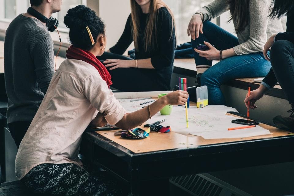 Grupo de adolescentes estudando juntos ao redor de uma mesa com cadernos e canetas coloridas